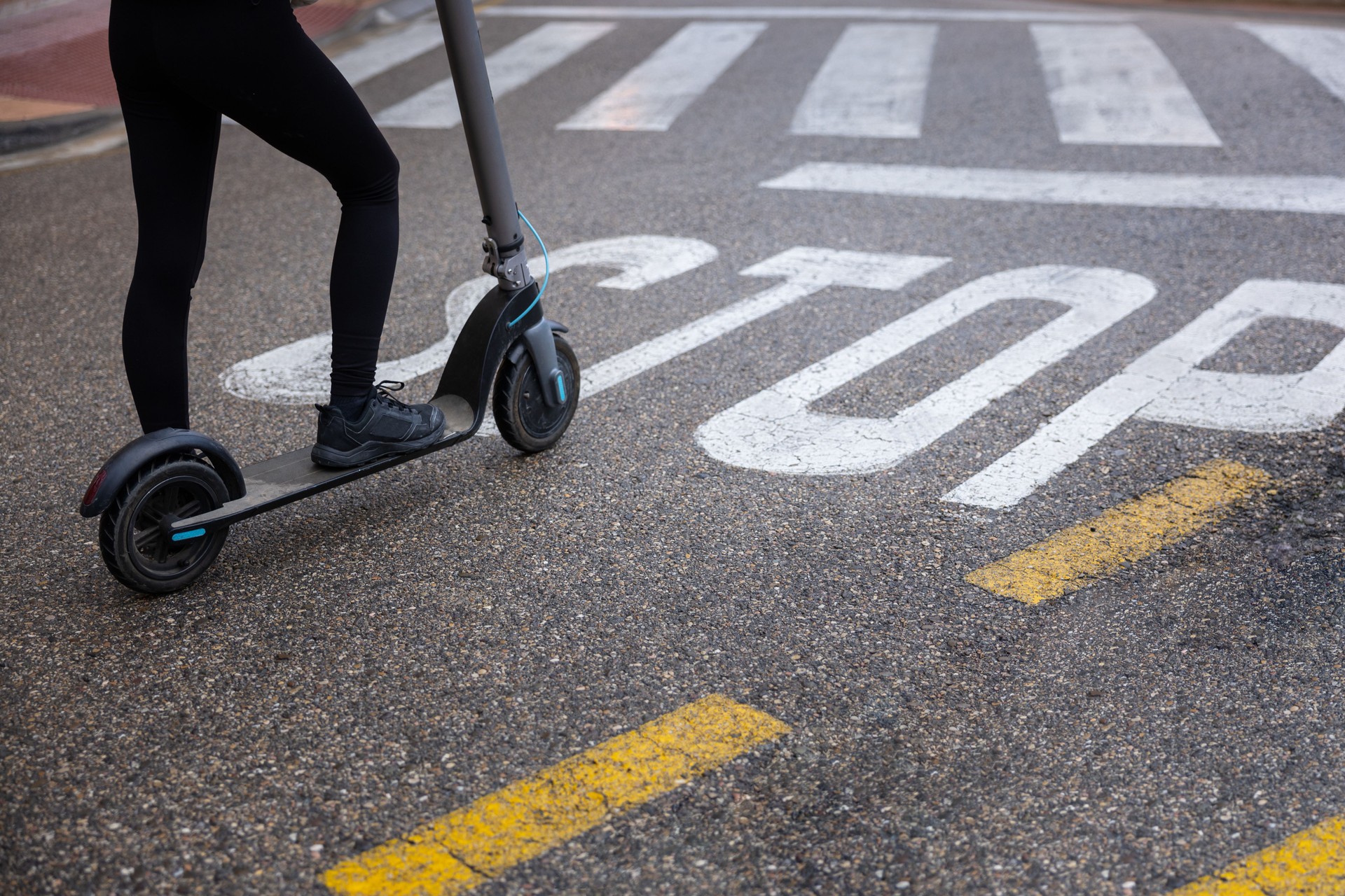 Young girlhalts at a STOP sign, showcasing the blend of traditional road signs and modern e-scooter transportation in an urban setting.